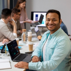 Smiling Indian man at a desk with laptop, representing financial expertise